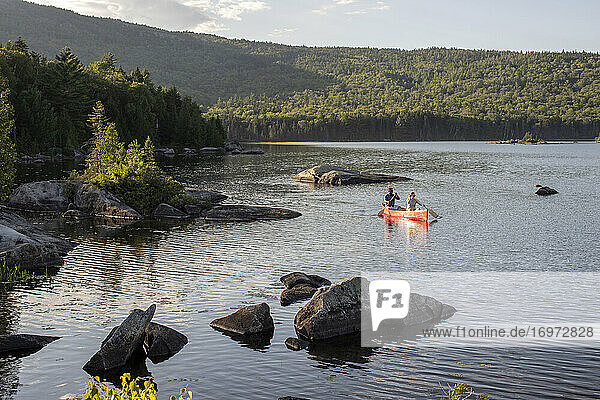 Ehepaar paddelt mit rotem Kanu zwischen Felsen auf einem See in der Wildnis von Maine