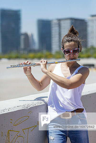 Woman with ponytail playing a flute while standing outdoors