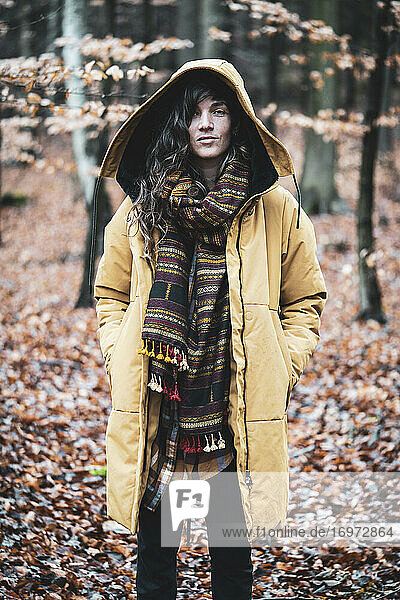 Strong young woman stands with hooded jacket in autumn leaves forrest