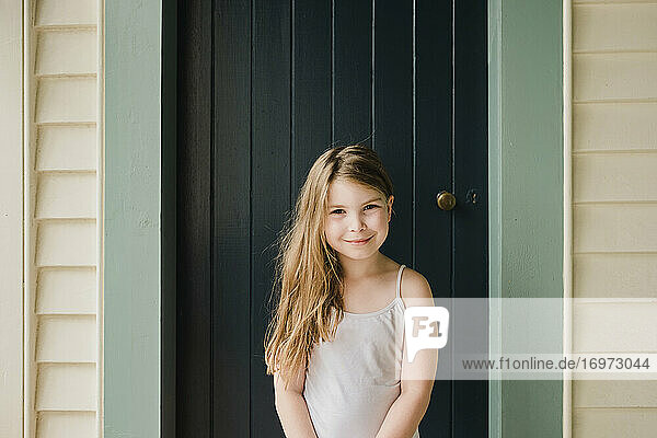 Lächelndes junges Mädchen steht draußen vor einer Tür