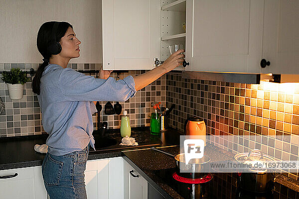 Woman putting dishware in cupboard in kitchen