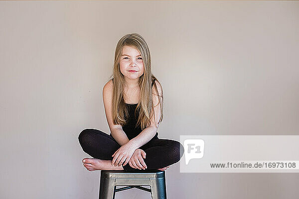 Close up of a young girl sitting cross legged on a stool