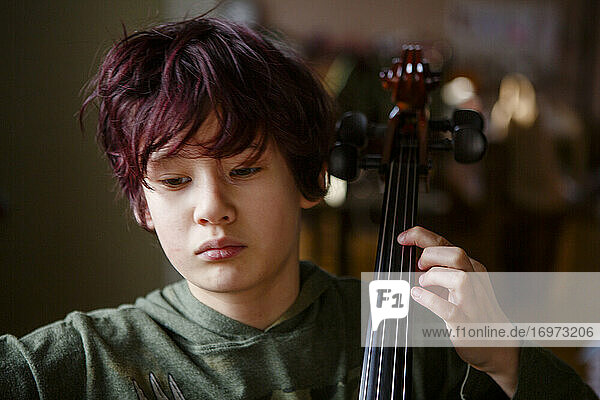 Nahaufnahme eines ernsten Jungen mit gefärbten roten Haaren beim Üben von Cellomusik