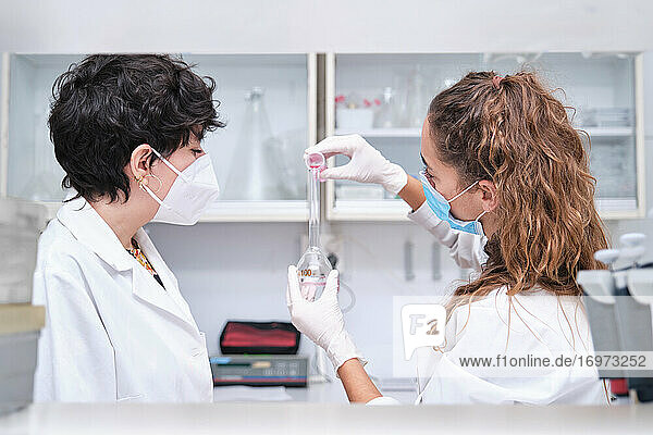 Zwei junge Wissenschaftlerinnen mit Gesichtsmasken  die einen Flachmann benutzen. Konzept der Laborforschung.