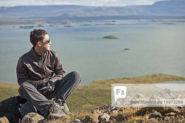 Jugendlicher  der sich auf dem Gipfel eines Berges über dem Myvatn-See in Island ausruht
