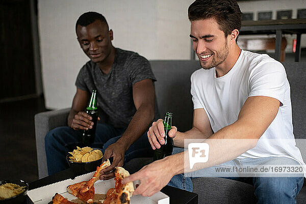 Fröhliche multiethnische Freunde essen Pizza und trinken Bier
