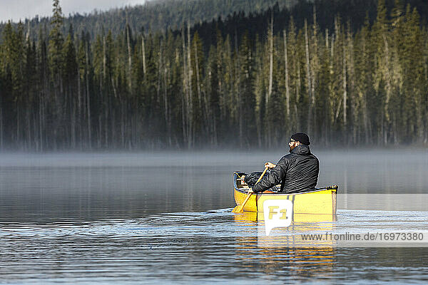 Bärtiger Abenteurer paddelt allein auf einem ruhigen  nebligen See in einem Kanu