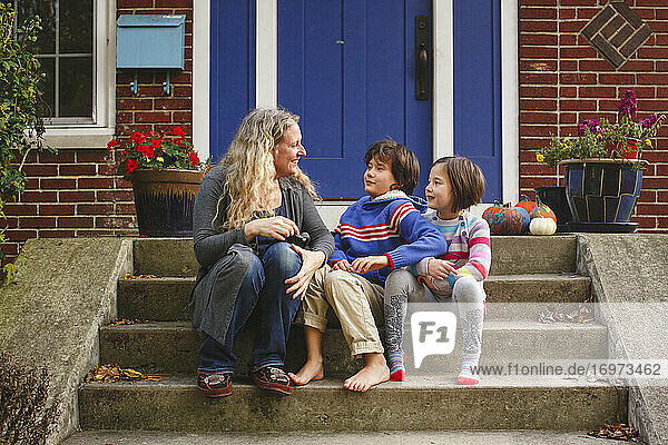 Eine lächelnde Mutter sitzt mit ihren beiden Kindern auf der vorderen Treppe ihres Hauses