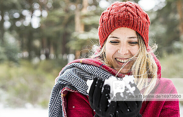 Porträt einer glücklichen jungen Frau  die im Winter mit Schnee spielt und Schneeflocken in die Kamera bläst  Kopierraum