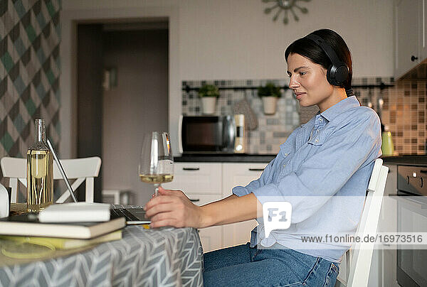 Woman with glass of wine taking rest and using laptop at home