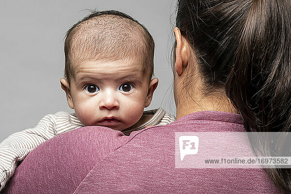 Ein Baby in den Armen seiner Mutter schaut ihr intensiv über die Schulter