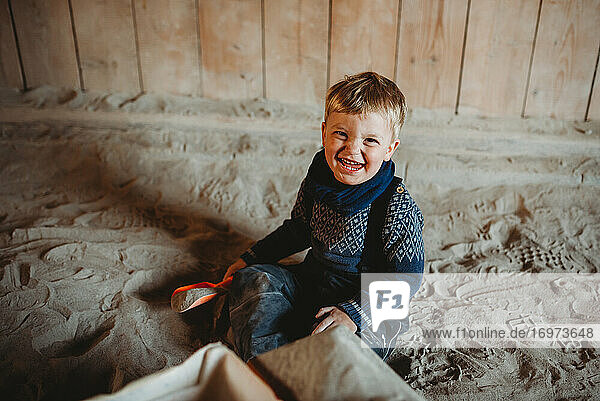 Kleiner Junge lächelnd spielen in Sand im Winter mit Schaufel in der Hand