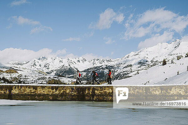 Gruppe von Wanderern auf Schneeschuhen überquert einen See vor schneebedeckten Gipfeln