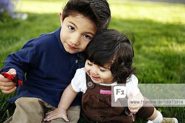 Young boy and his toddler sister looking at camera  in the park