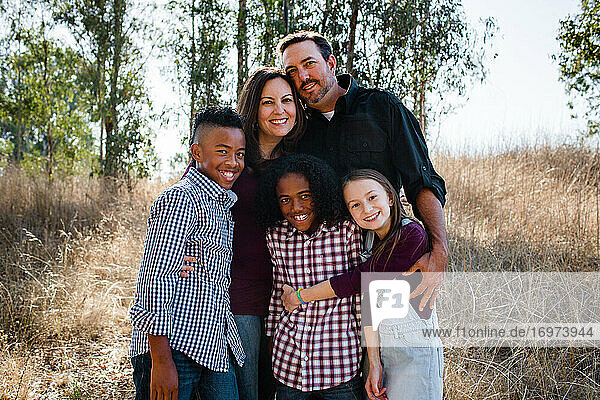 Fünfköpfige Familie im Feld stehend und für die Kamera lächelnd