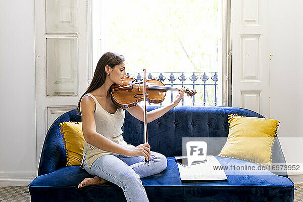 Musikerin spielt zu Hause auf einem Sofa mit einem Tablet Bratsche.