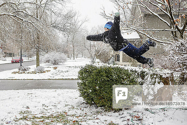 Junge springt sportlich in der Luft von einem schneebedeckten Felsen im Winter