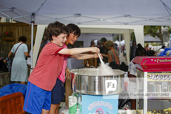 Zwei lächelnde Jungen machen gemeinsam Zuckerwatte auf einem Straßenfest im Sommer
