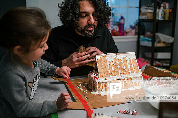 Father and daughter building gingerbread house at kitchen table