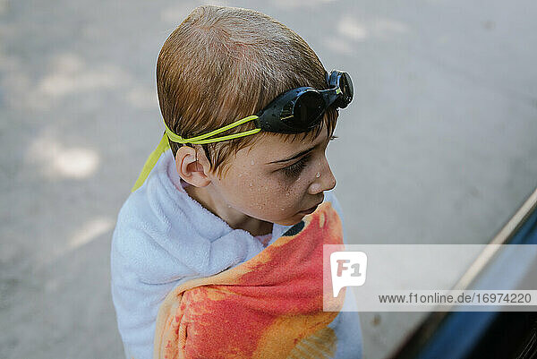 Boy wrapped in towel with goggles on his head and wet hair