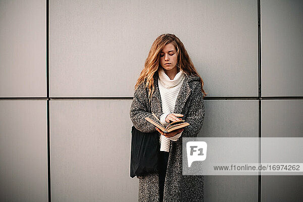 Porträt einer Studentin  die ein Buch hält und an einer grauen Wand steht