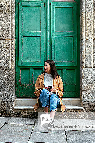 Junge stilvolle Frau  die im Freien sitzt und ein Smartphone benutzt