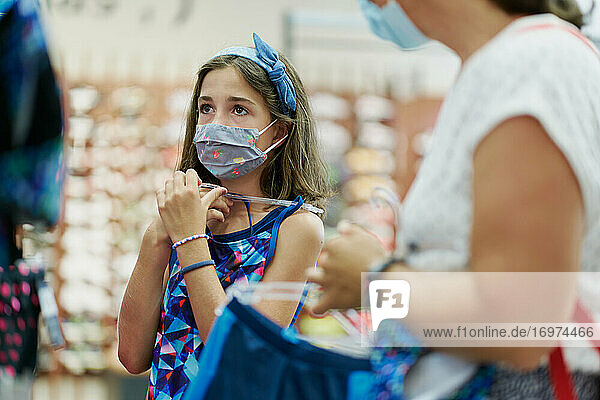 Mother and daughter wearing medical masks choosing a dress in a