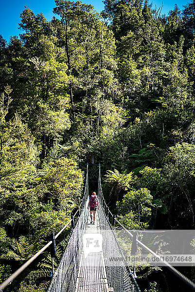 Frau geht über eine Hängebrücke auf dem Abel Tasman Coast Track