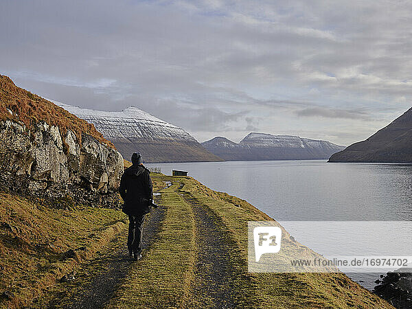 Frau geht auf der Straße entlang einer Bucht auf den Färöer Inseln