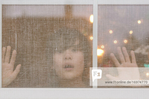 Ein kleiner Junge drückt sein Gesicht und seine Hände an ein vergittertes Fenster