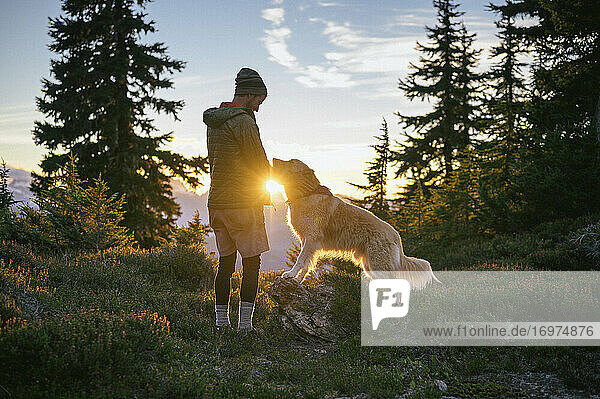 Male Hiker Petting Dog at Sunset With Sunburst