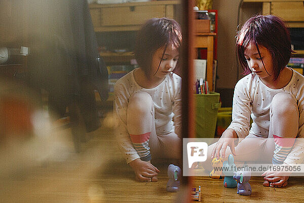 Ein kleines Kind sitzt gespiegelt im Glas und spielt mit Spielzeug auf dem Holzboden