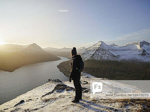 Frau auf verschneitem Berg mit Blick auf das Meer auf den Färöer Inseln