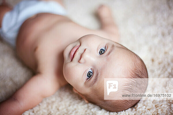 Baby boy laying on carpet and looking at the camera.