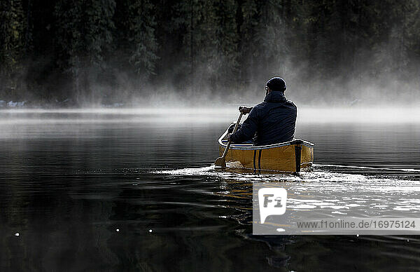 Bärtiger Abenteurer paddelt allein auf einem ruhigen  nebligen See im Kanu