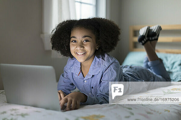 Zehnjähriges gemischtrassiges Mädchen arbeitet an einem Apple-Laptop und lächelt in die Kamera