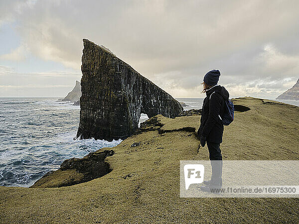 Frau blickt auf den Meeresstapel Drangarnir auf den Färöer Inseln