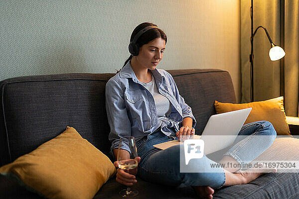 Junge Frau trinkt Wein und schaut sich zu Hause einen Film auf dem Laptop an