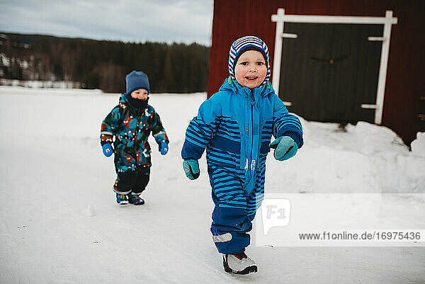 Junge Zwillingsjungen lächelnd zu Fuß im Schnee in skandinavischen Bauernhof von Scheune