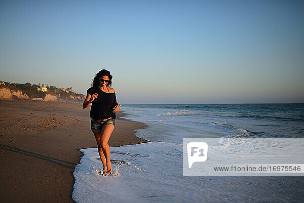 Junge Frau läuft bei Sonnenuntergang am Strand