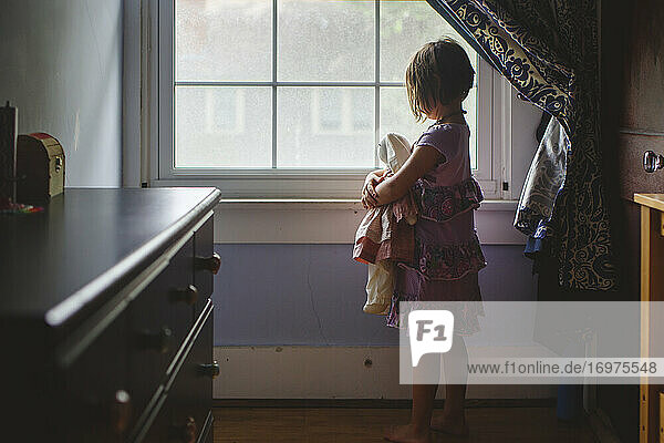 Porträt eines kleinen Kindes  das allein im Schlafzimmer steht und ein Stofftier hält