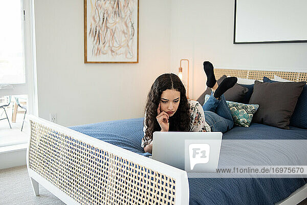 Junge Frau liegt auf dem Bett und schaut auf einen Laptop