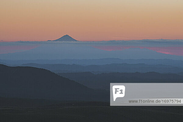 Der Gipfel des Mt Taranaki erhebt sich über die Wolken  während die Sonne hinter dem Horizont untergeht  Tongariro  Neuseeland