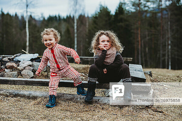 Bruder und Schwester sitzen auf einem Holzklotz draußen im Wald im Winter
