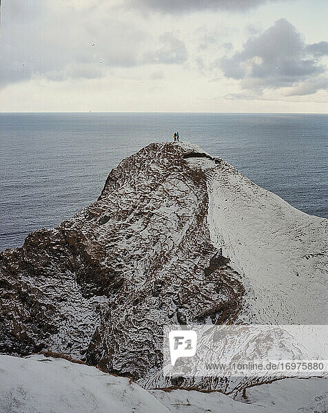 Zwei Menschen stehen am Rande einer verschneiten Klippe auf den Färöer-Inseln
