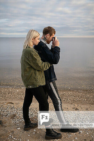 Junges Paar mit Fotokamera am Seeufer stehend