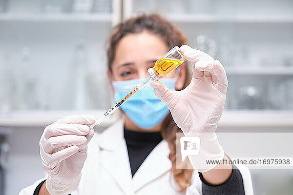 Junge Wissenschaftlerin mit Gesichtsmaske  die eine Ampulle mit Coronavirus-Impfstoff  Spritze und Nadel hält. Entwicklung des Impfstoffs Covid-19.