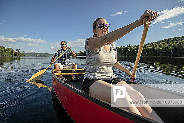 Weiße Frau und schwarzer Mann paddeln mit einem roten Kanu auf einem Waldsee in Maine