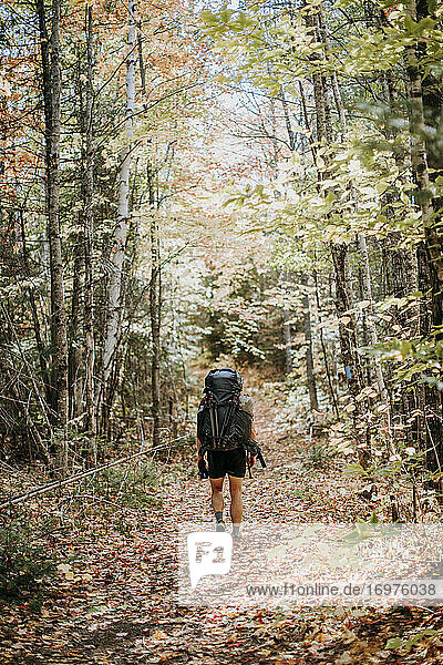 Mann wandert mit voll beladenem Rucksack auf einem Waldweg in Maine