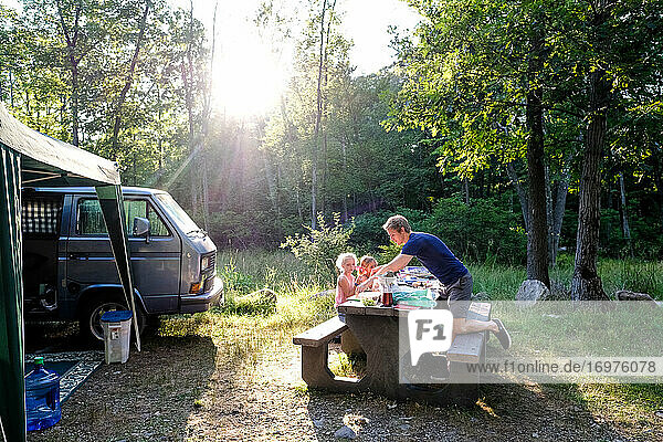 family sitting together at dinner while camping in woods in summertime